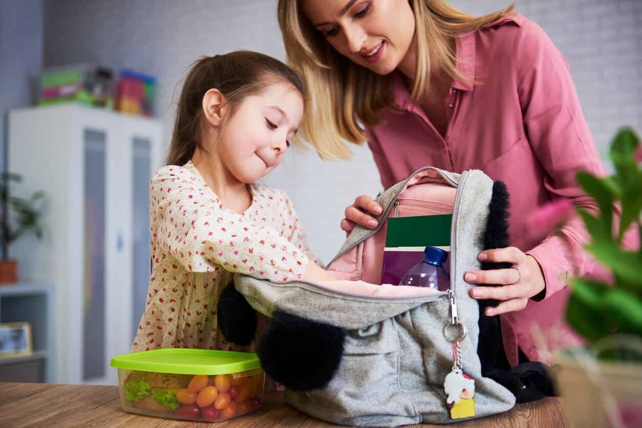 Une jeune fille qui prépare son cartable avec sa maman.