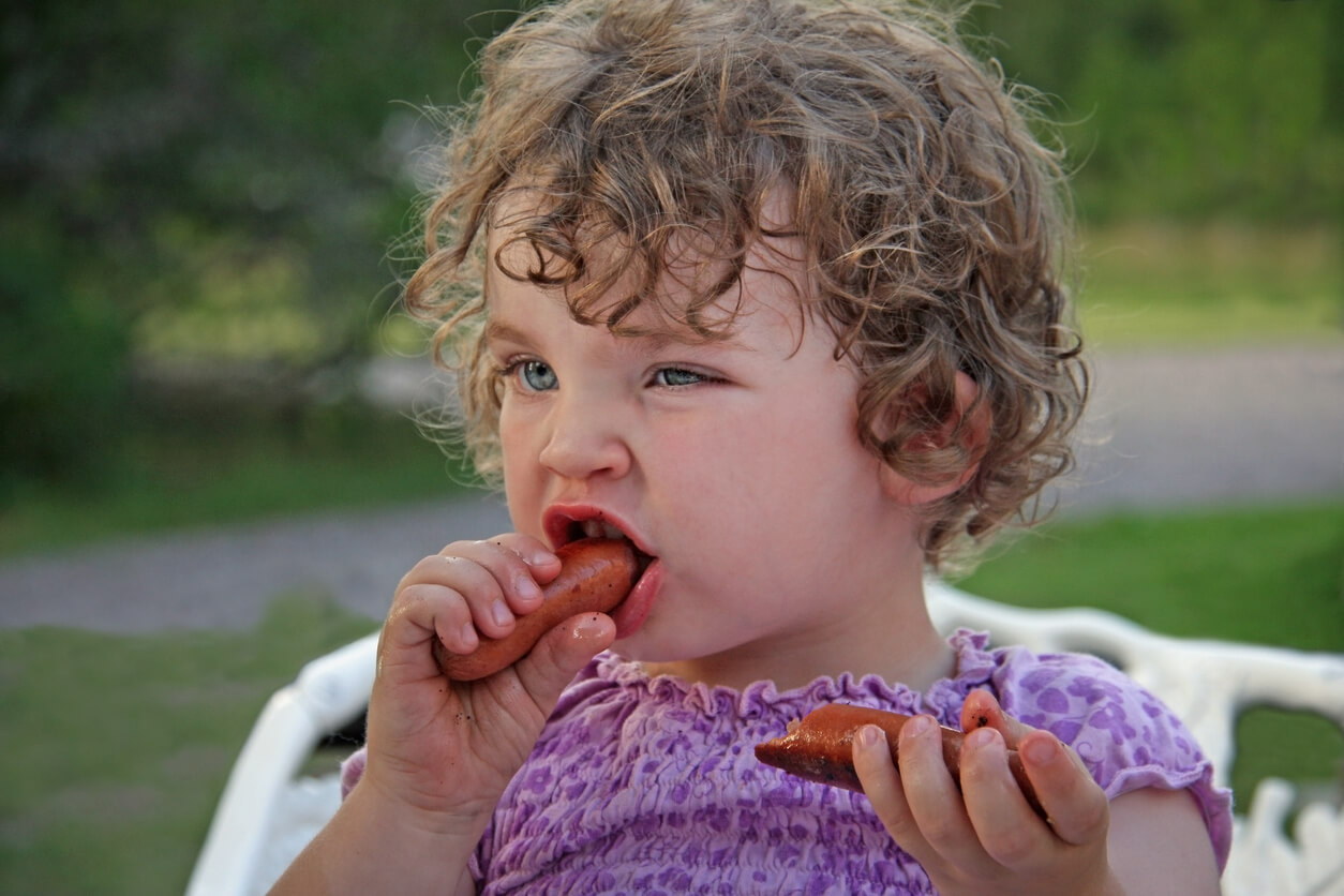 A young child eating a sausage.