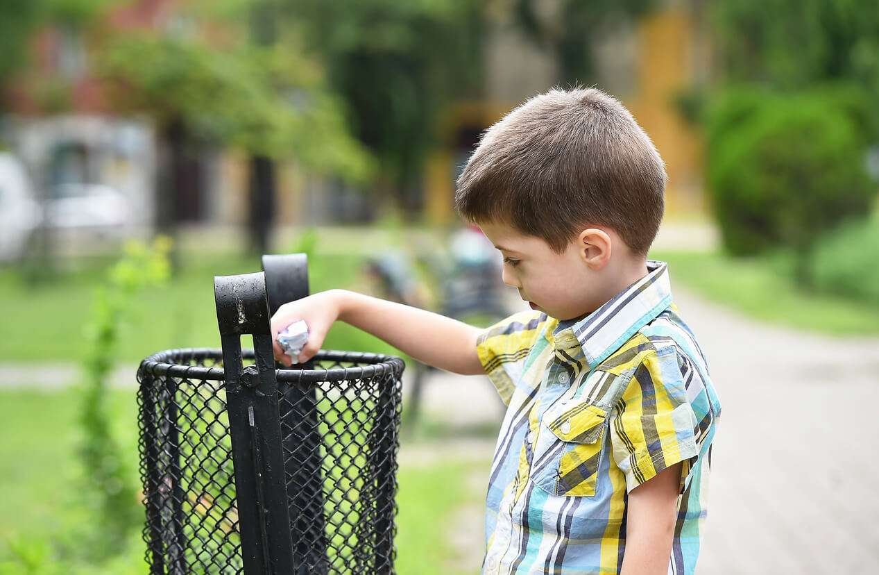 A child throwing away trash in a garbage can at the park.
