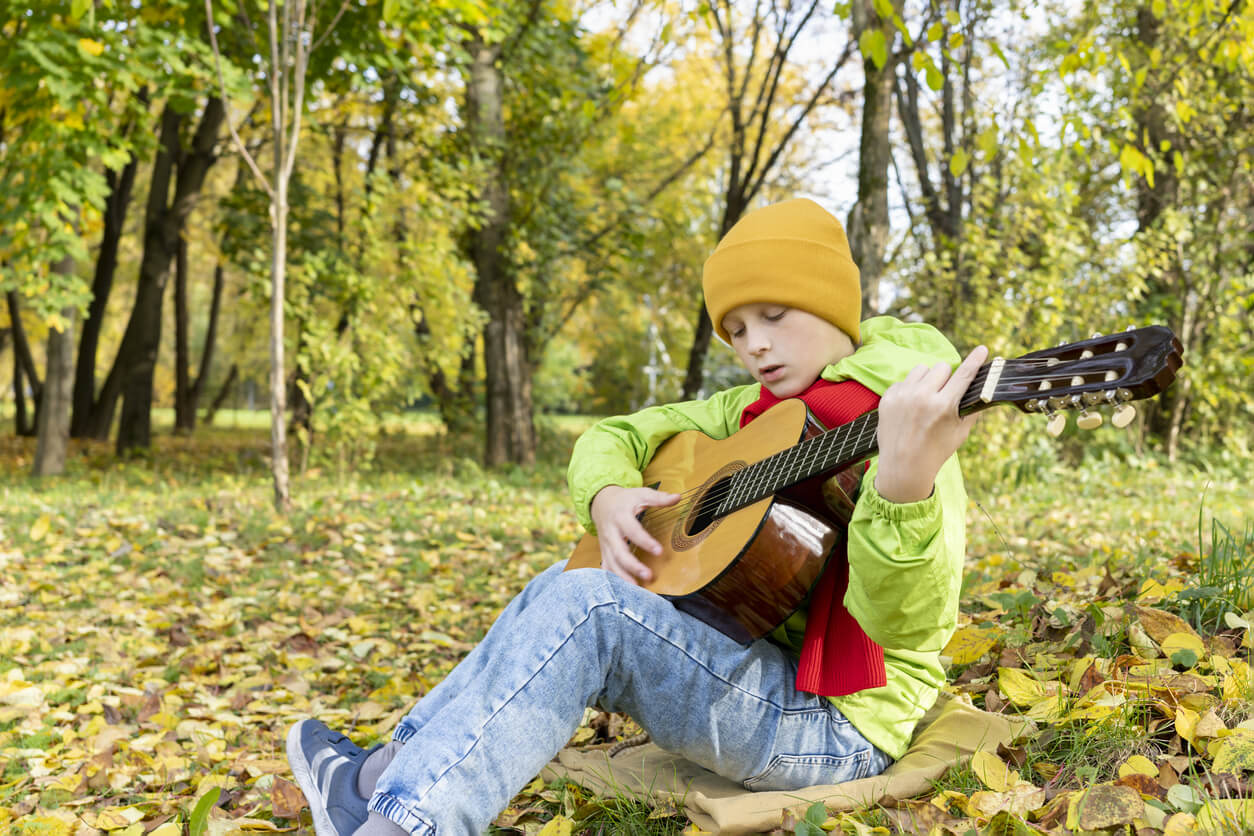A young boy sitting on the ground playing the guitar.