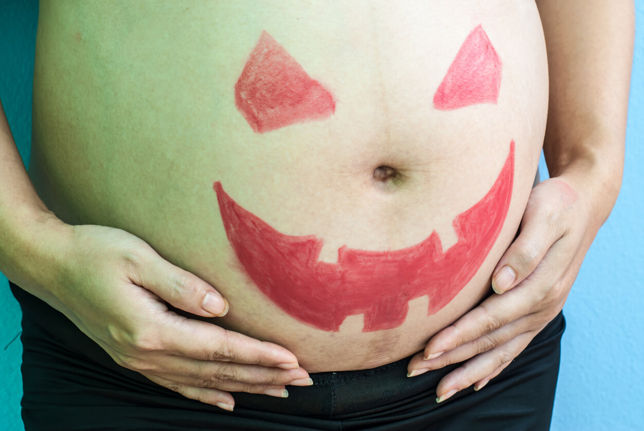 A woman with the face of a jack-o-lantern on her pregnant belly.