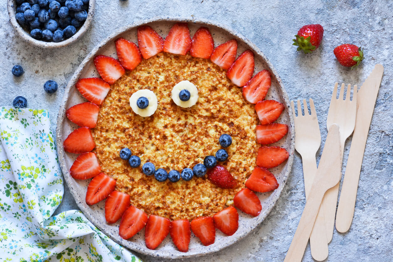 A whole grain pancake decorated like a smiley face with fruit.
