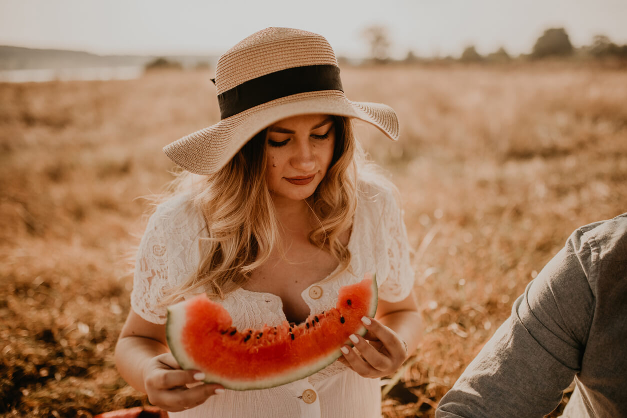 A pregnant woman eating watermelon while on a picnic.