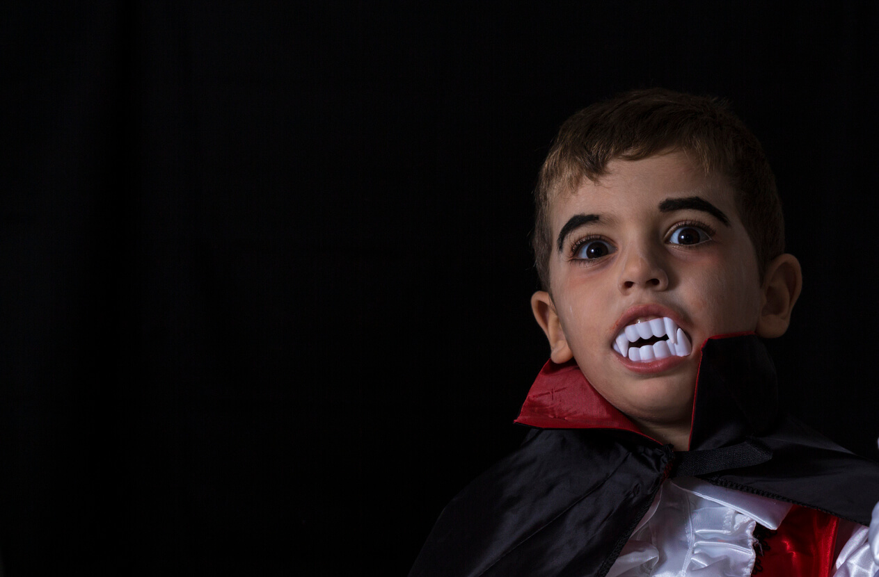A child dressed up as a vampire wearing fake vampire teeth.