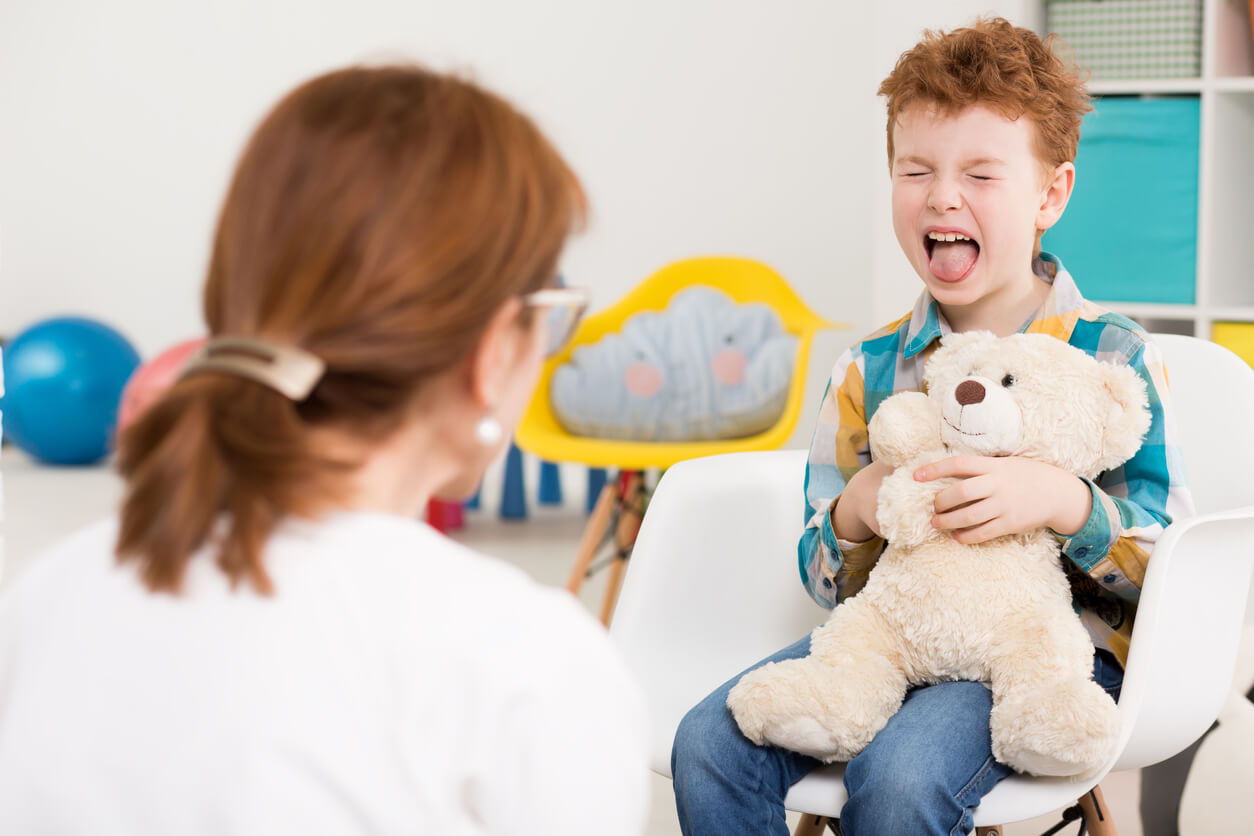 A child sticking out his tongue and holding a teddy bear during a therapy session.