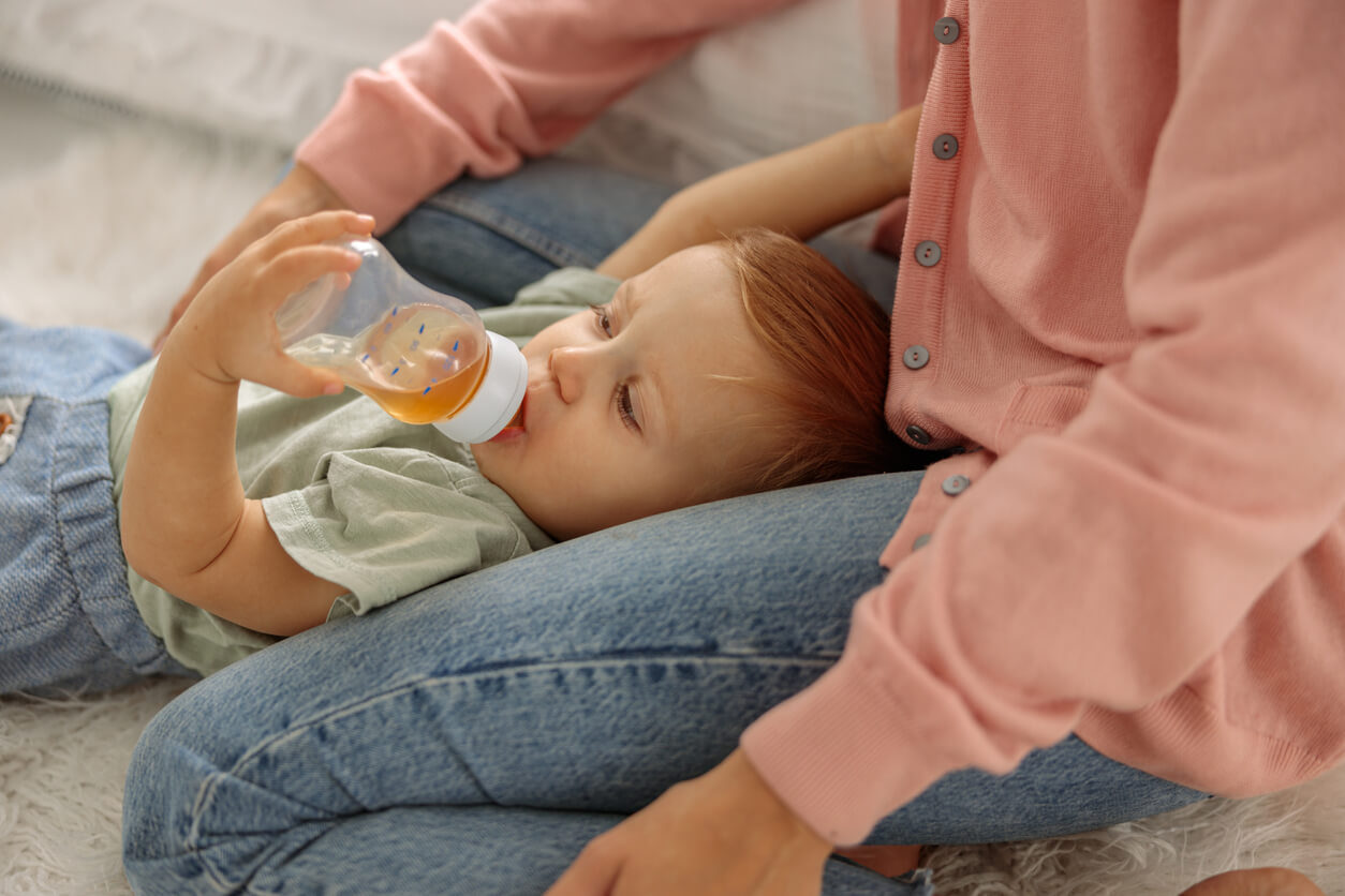 A baby lying on his mother's lap, drinking tea from a bottle.