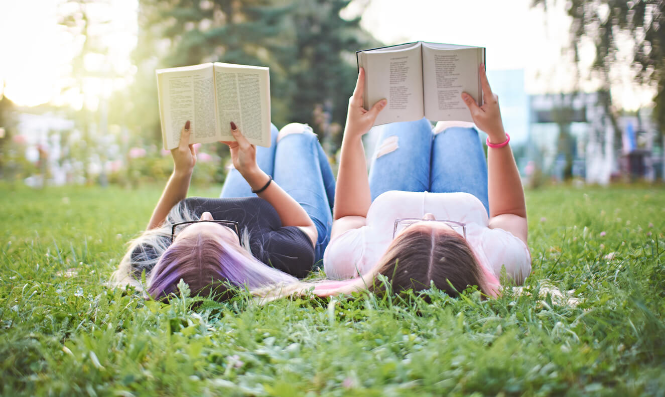 Deux adolescentes qui lisent un livre allongées dans l'herbe.