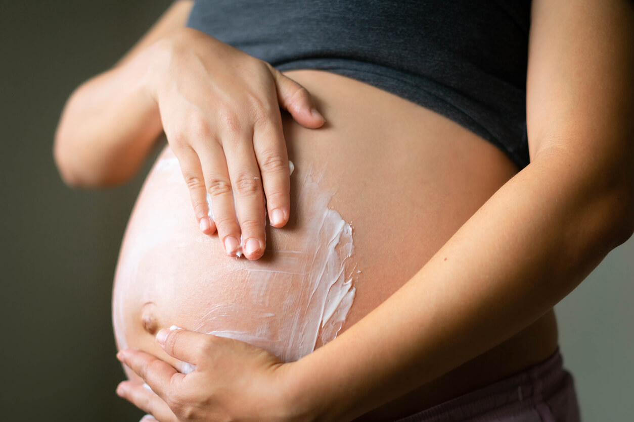 A woman rubbing lotion onto her pregnant body.