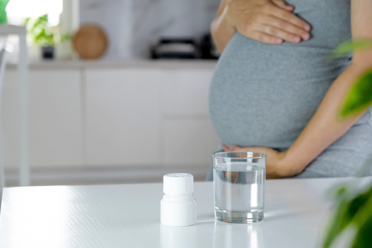 A woman standing by a pill bottle and a glass of water.