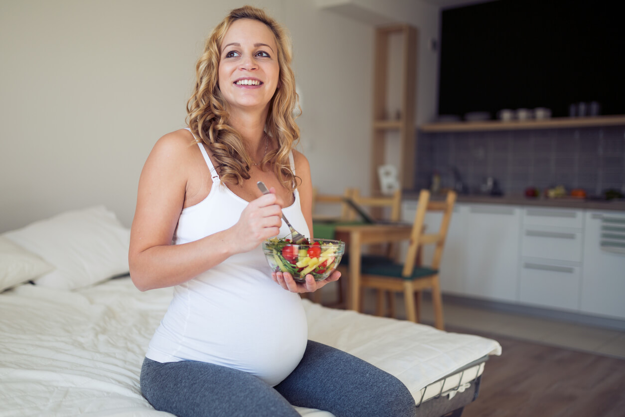 A pregnant woman eating a fresh salad.