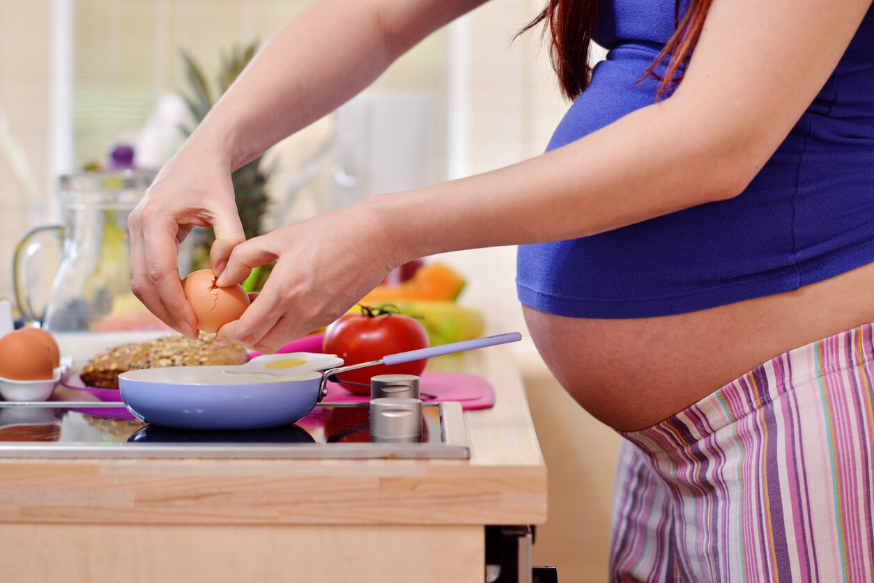 A pregnant woman breaking an egg into a frying pan.