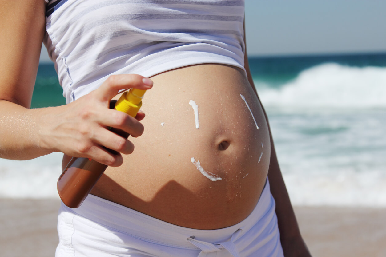 A pregnancy woman putting sunscreen on her belly at the beach.