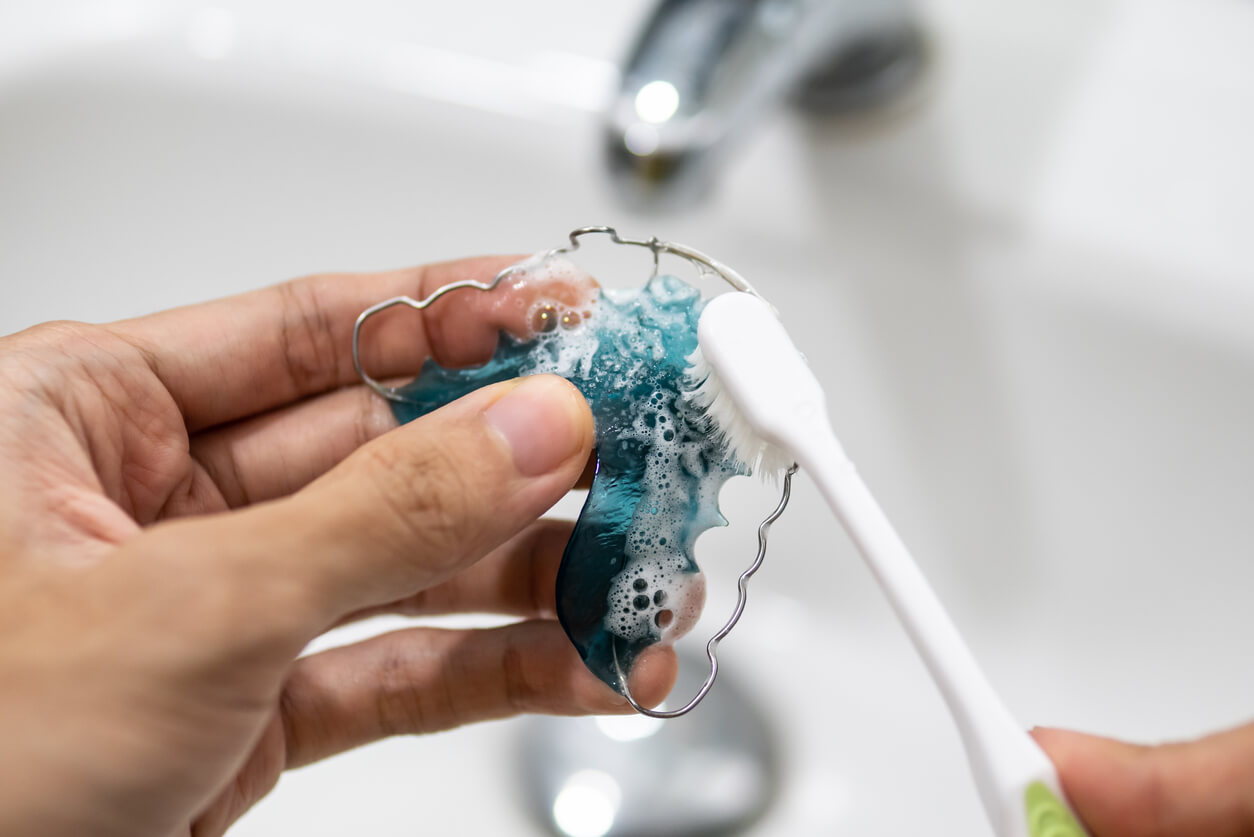 A person brushing a removable orthodontic appliance with a toothbrush.