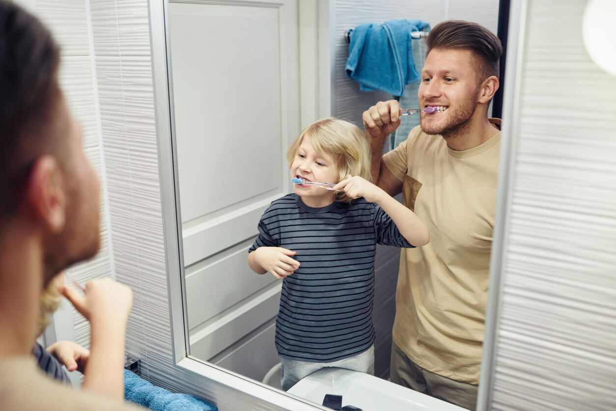 A father and son looking in the mirror as they both brush their teeth.