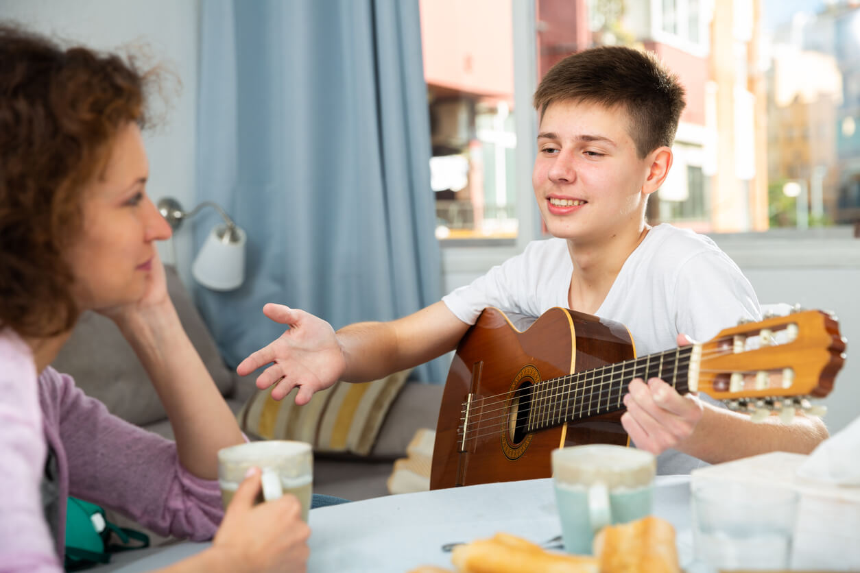 A teenage boy talking to his mother about playing the guitar.