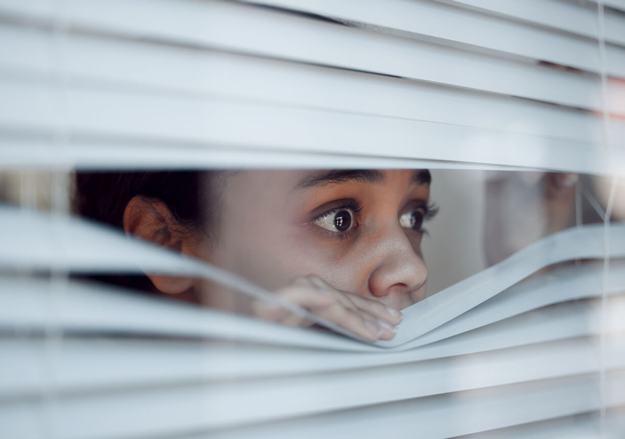 Teini-ikäinen katsoo peloissaan ulos ikkunasta.