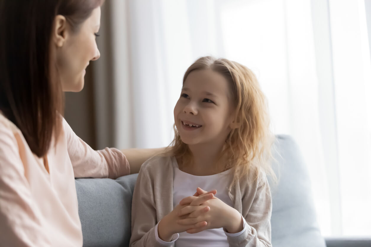 A mother and her young daughter talking about school while sitting on the couch.
