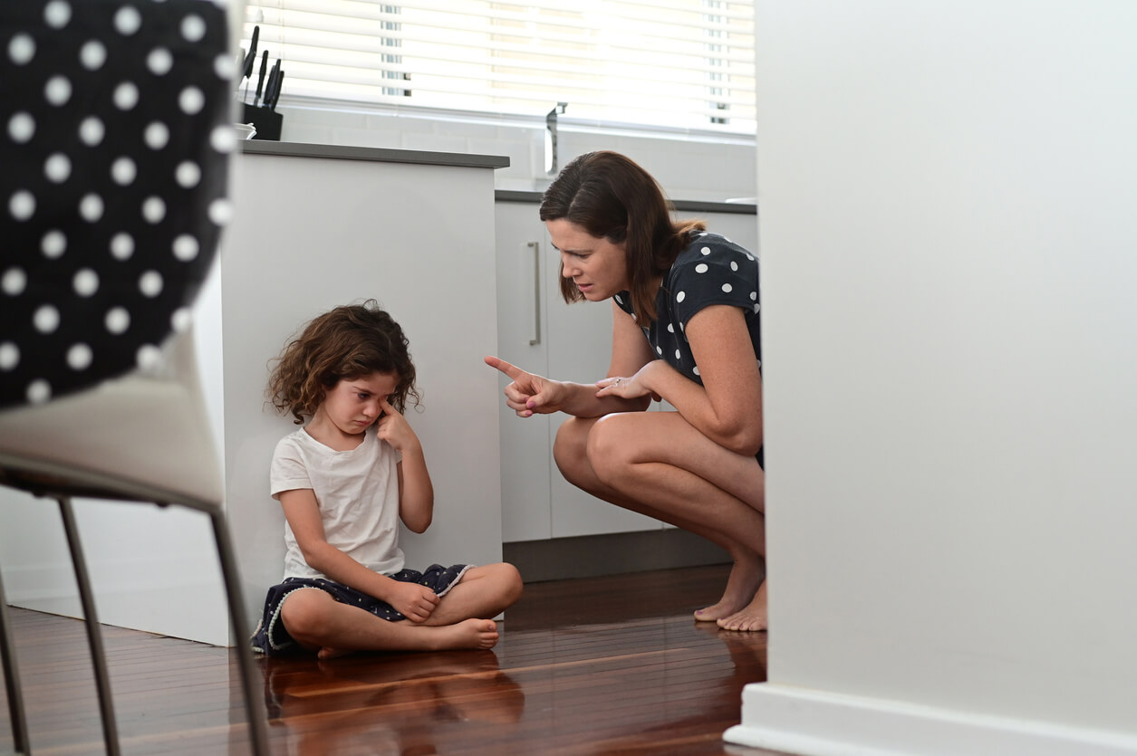 A mother scolding her young duaghter, who's sitting on the floor crying.