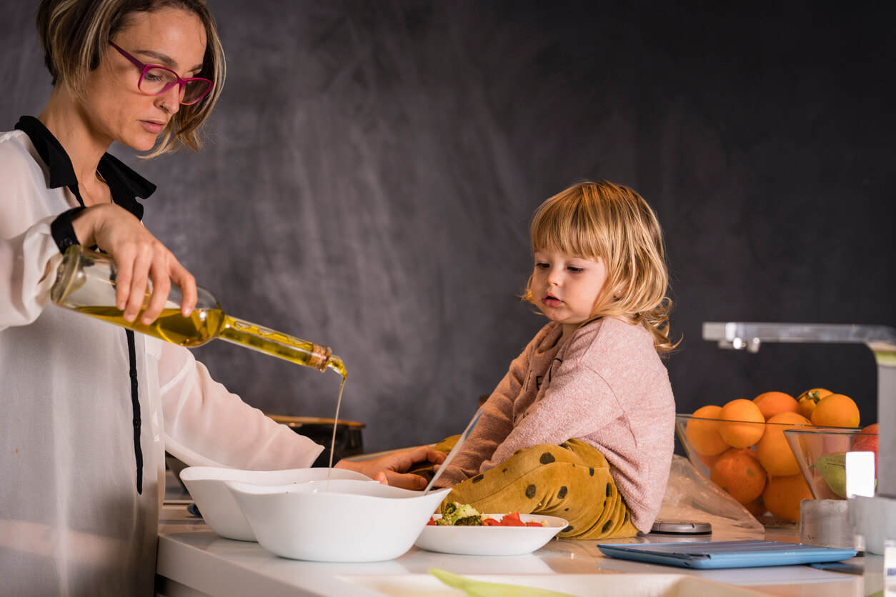 Une femme qui cuisine avec de l'huile d'olive devant une jeune fille.