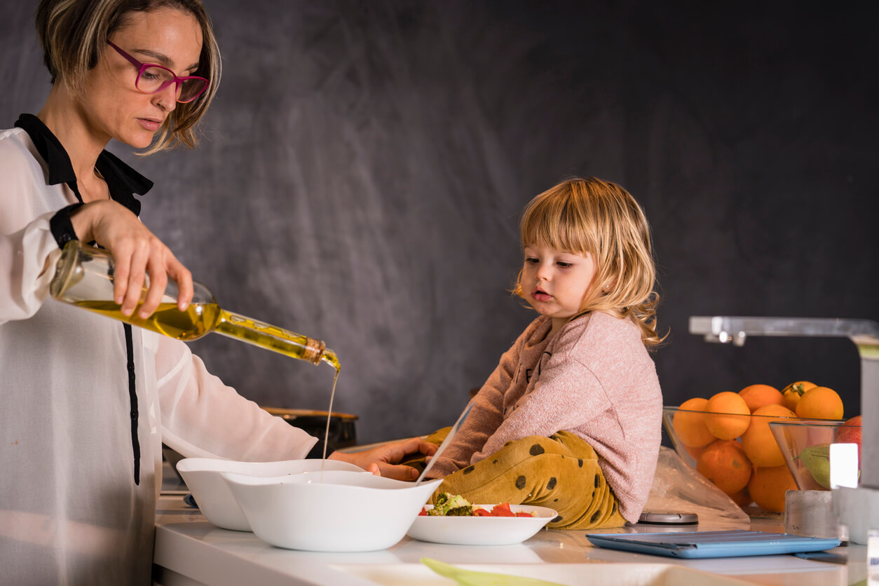 A mother preparing food for her toddler daughter with olive oil.