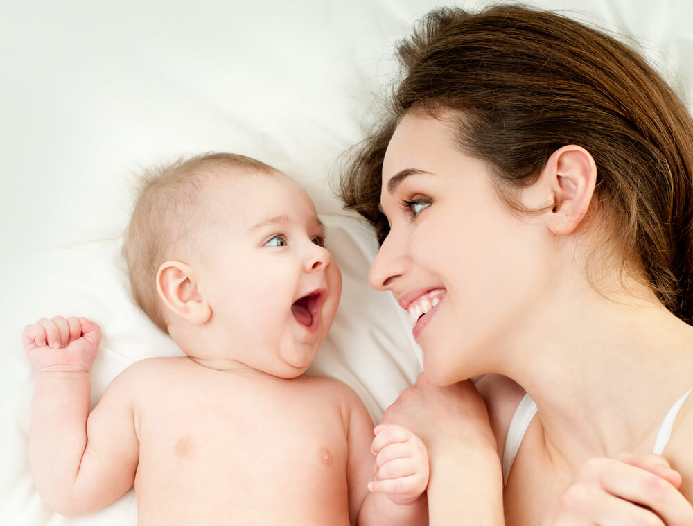 A mother smiling at her baby in bed.