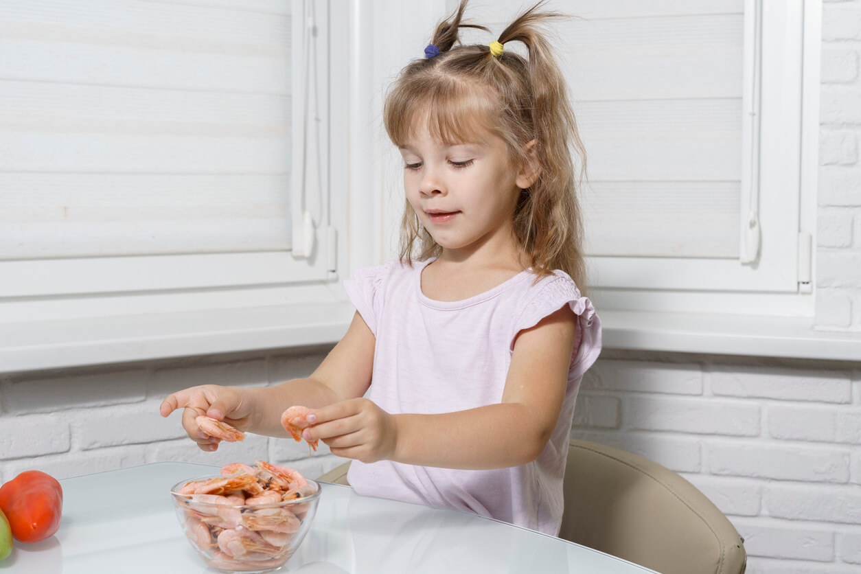 A young girl picking up shrimp from a bowl.