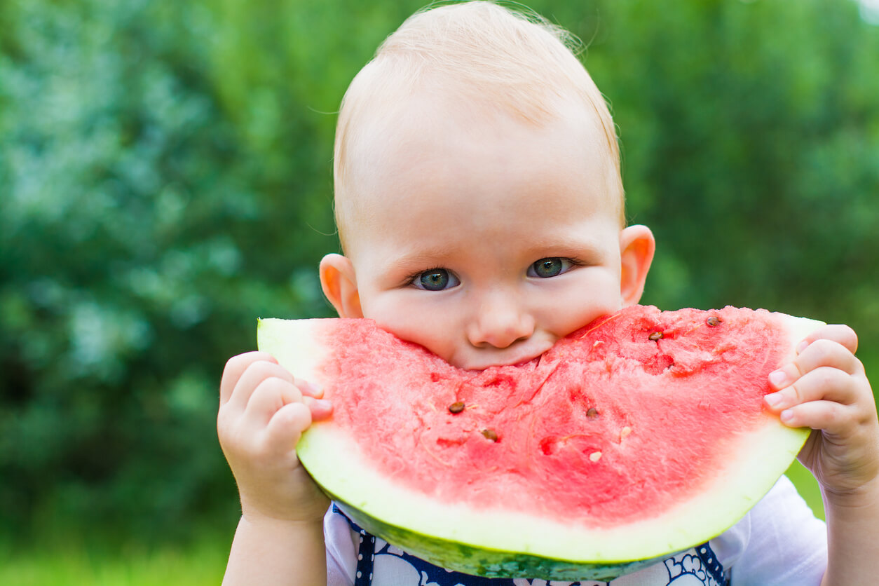 A baby biting into a watermelon slice.