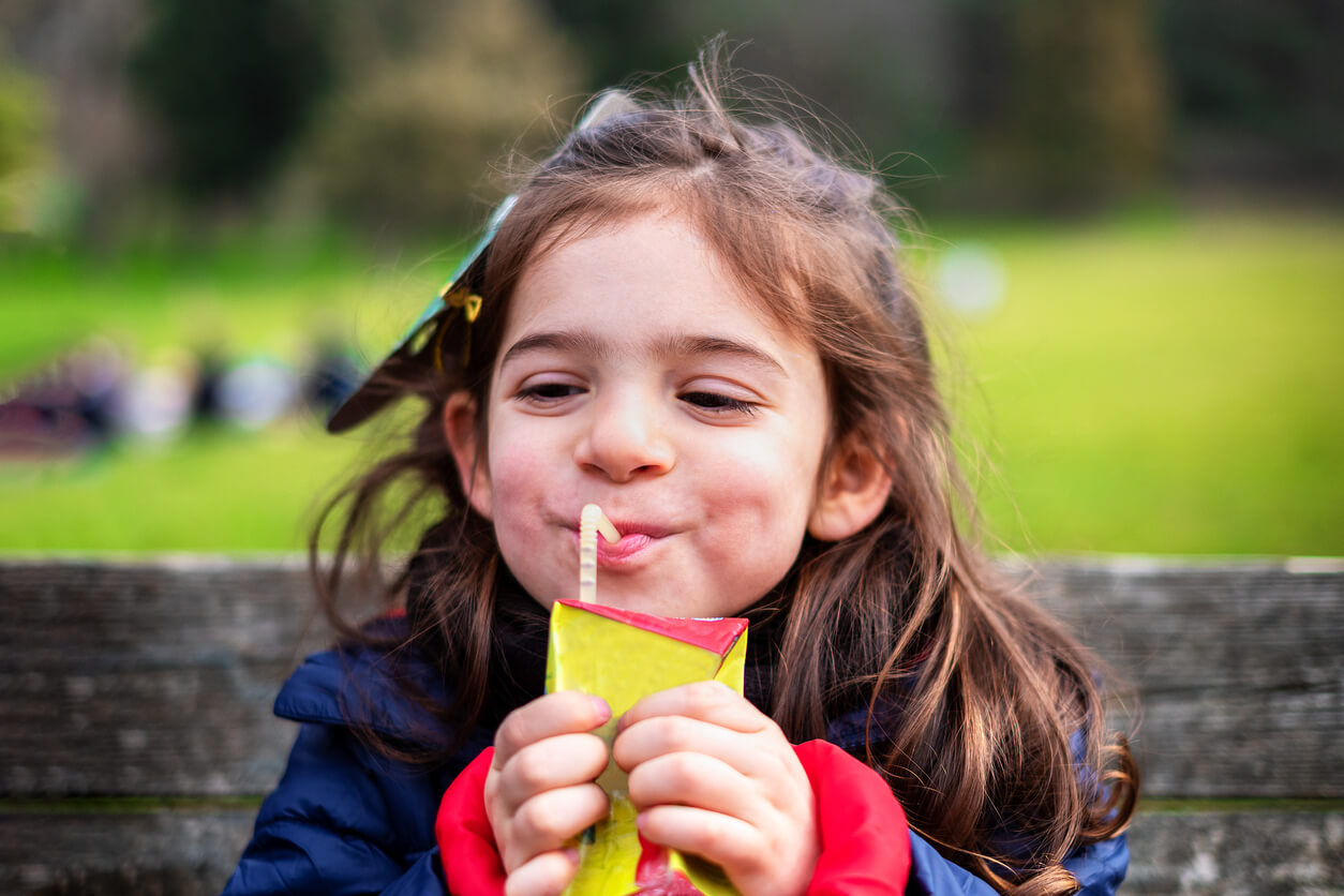 A young girl drinking from a juice box.