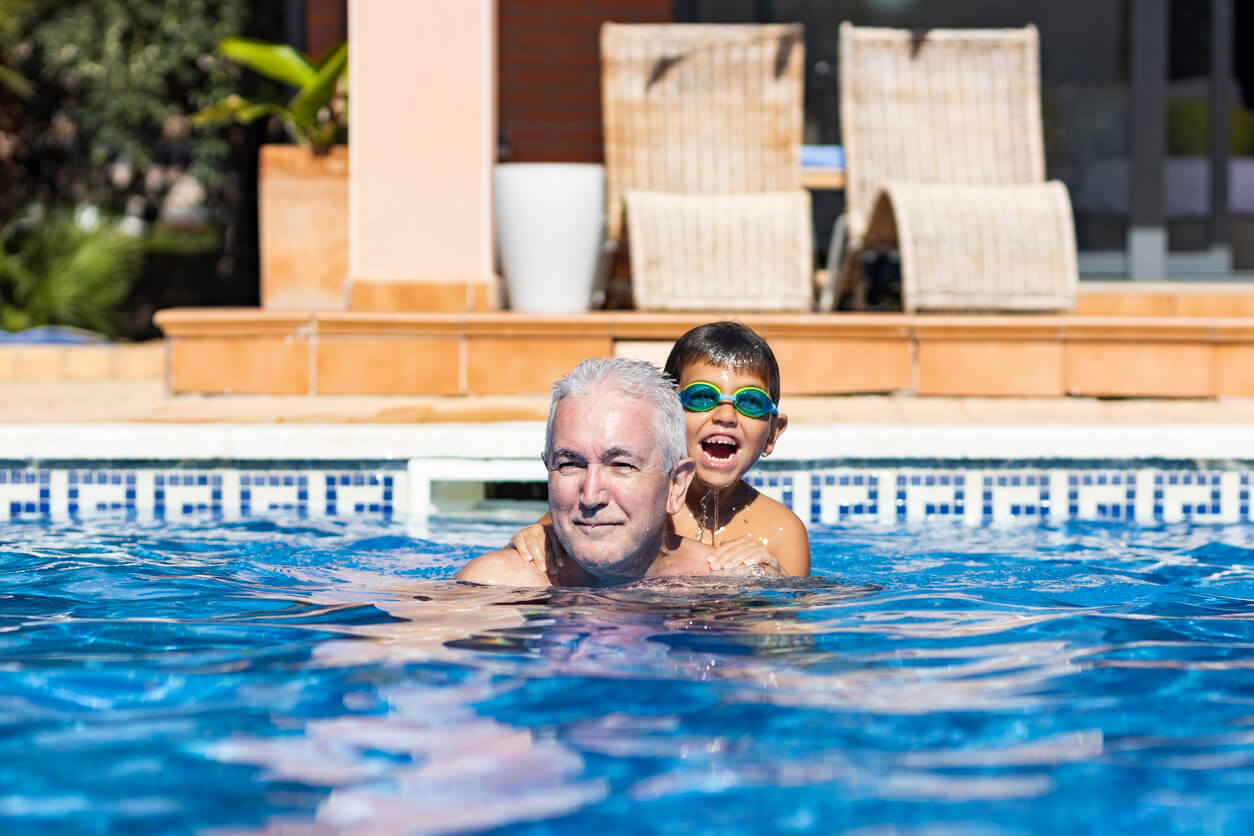 En gutt svømmer i bassenget med bestefaren sin.