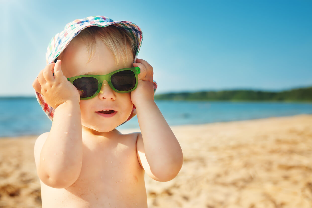 A baby wearing sunglasses at the beach.