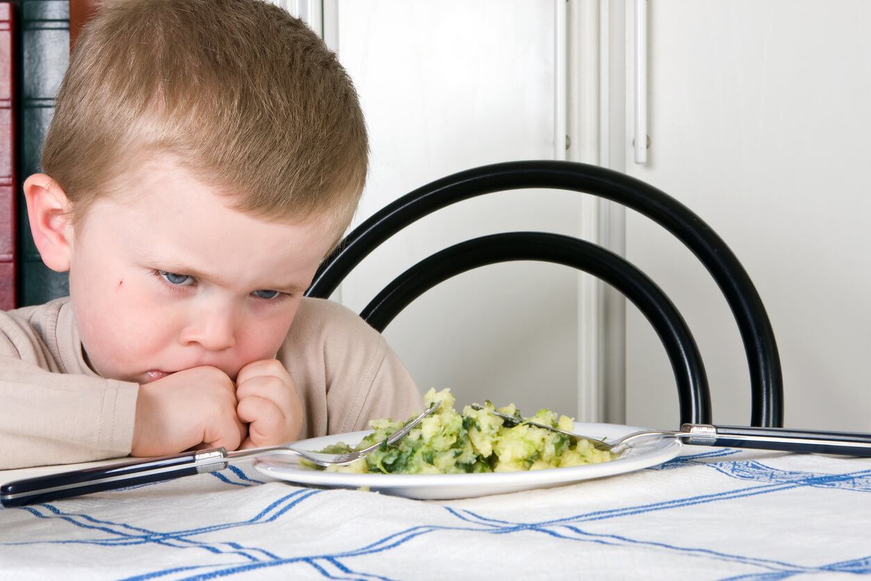A small child sitting at the table refusing to eat.