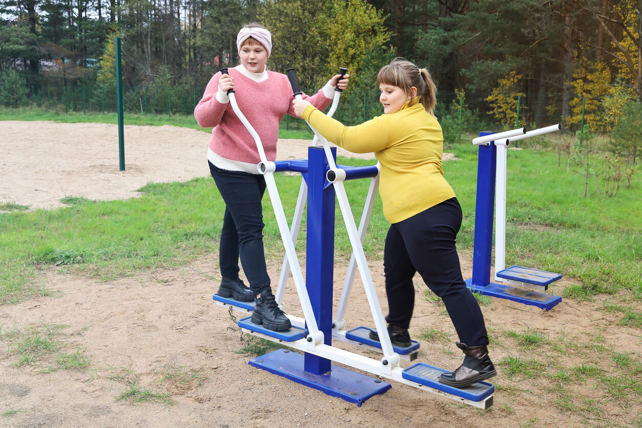 Two overweight girls using exercise equipment at the park.