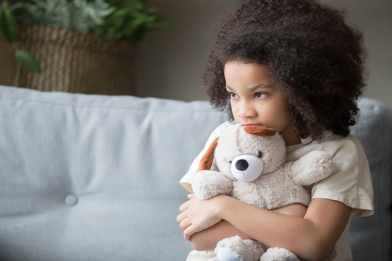 A young girl hugging her teddy bear and looking sullen.