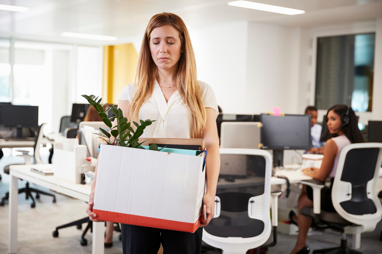 Une femme triste dans son bureau de travail avec un carton dans les bras. 