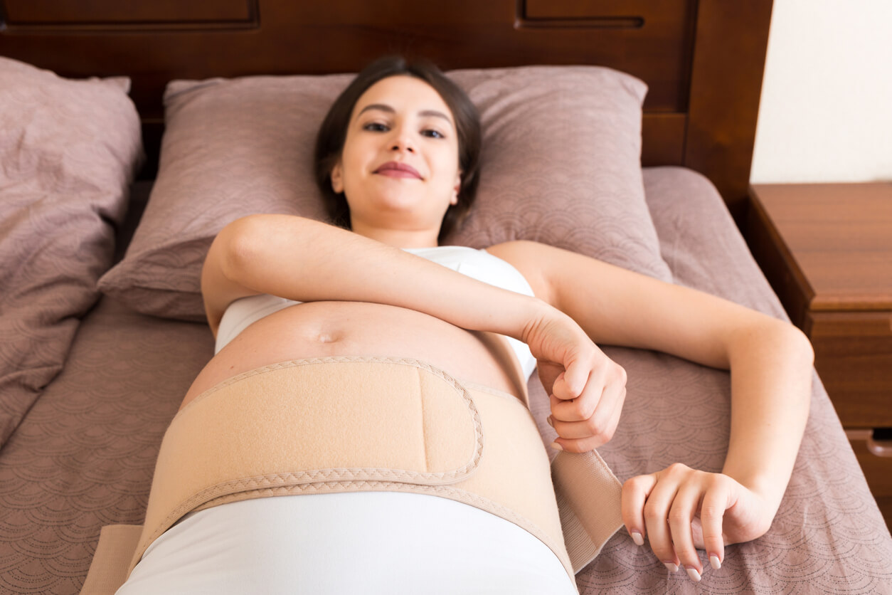 A pregnant woman lying in bed putting on a belly band.