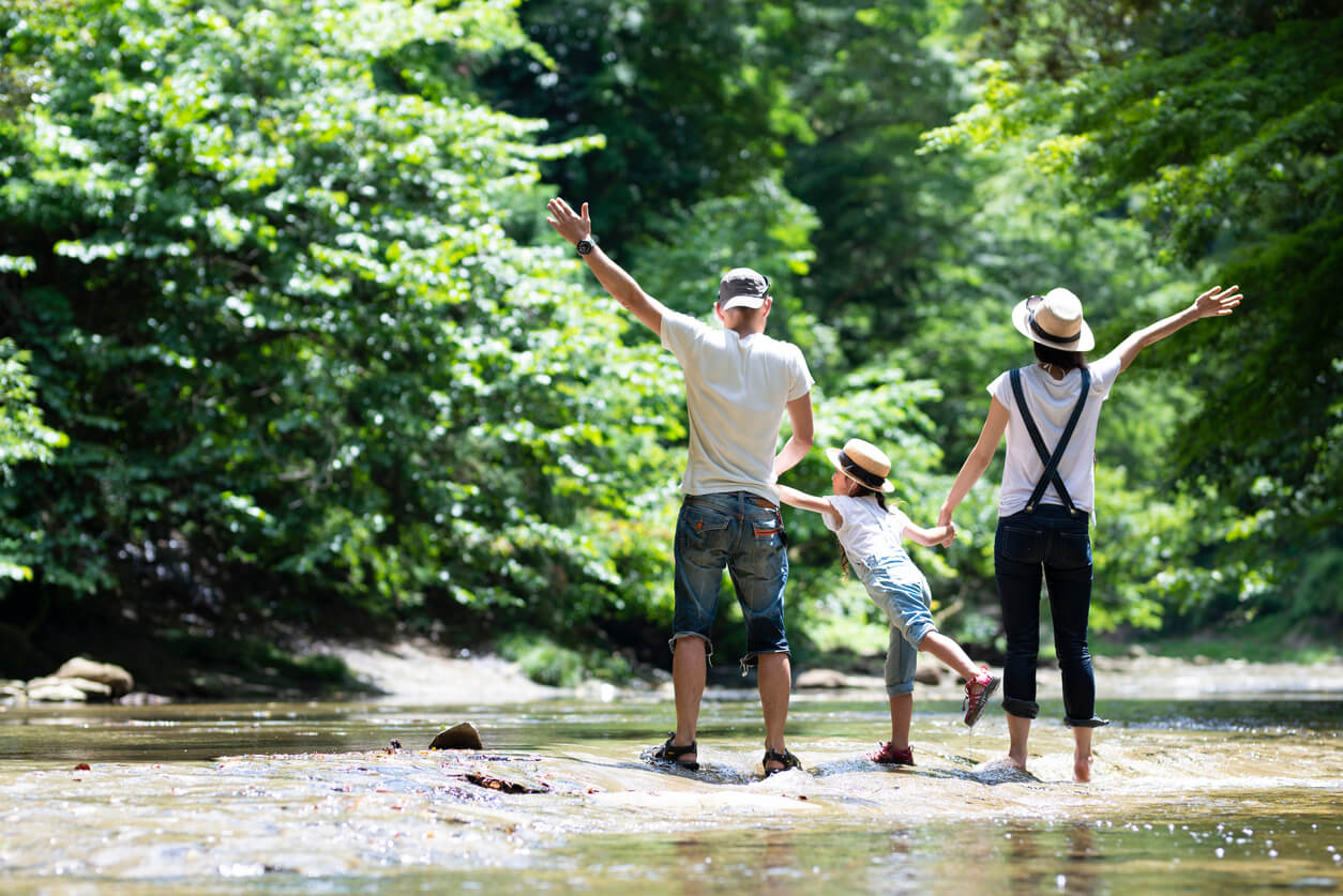 A family of three standing by a forest stream.