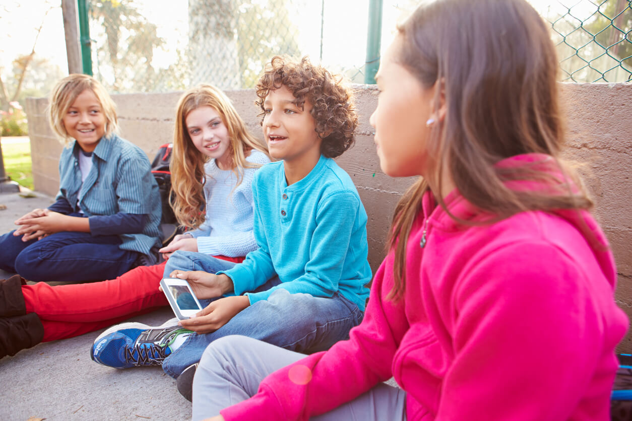 pre-teens sitting on the ground talking.