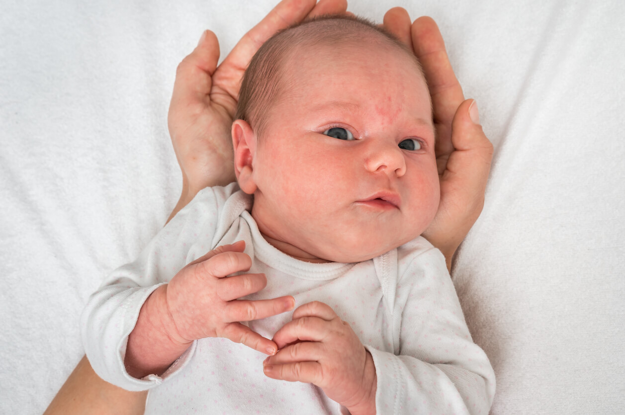 En nyfødt baby hviler hodet i en voksens hender.
