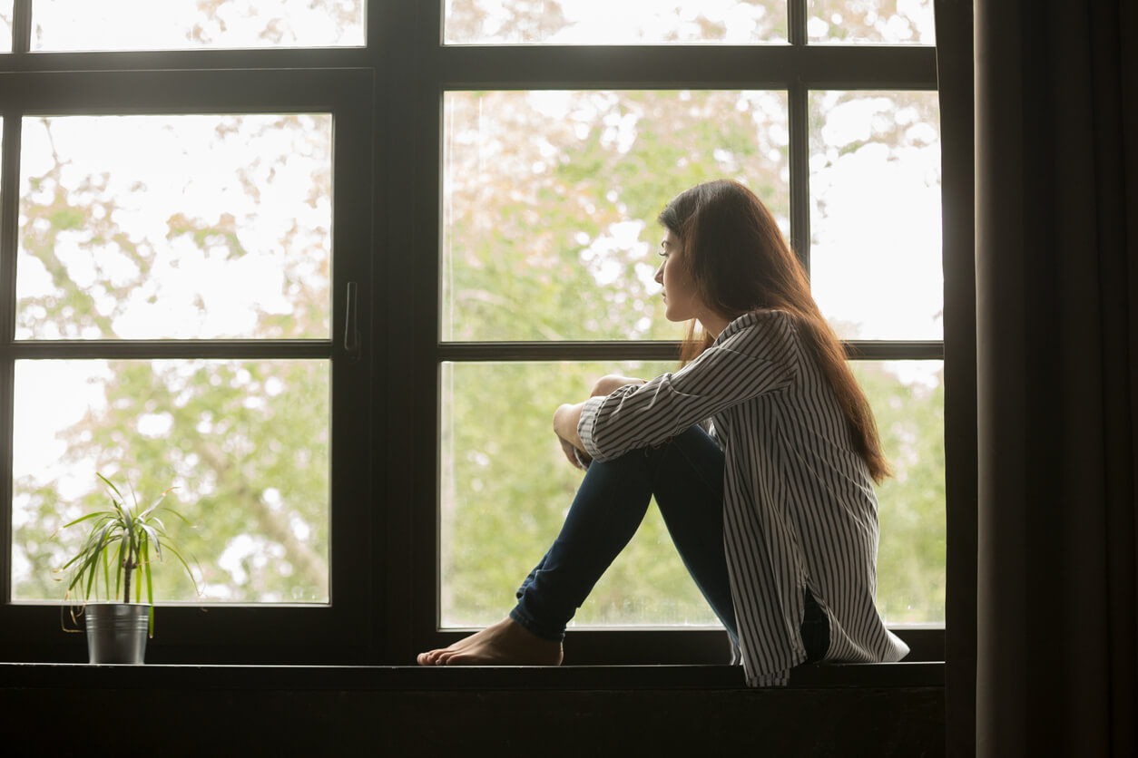 Une jeune femme assise devant une fenêtre qui regarde dehors. 