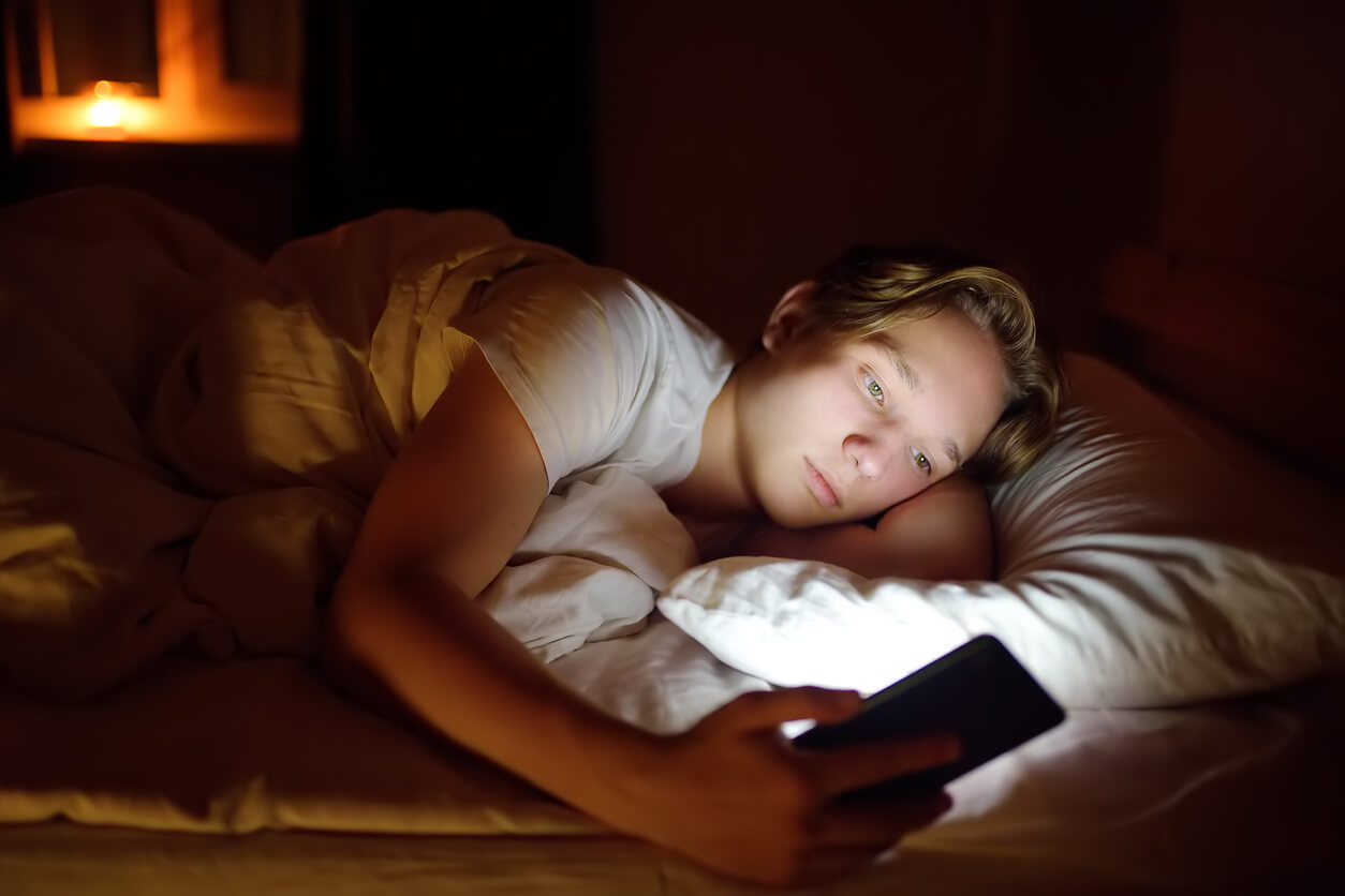 En pojke tittar på mobilen i sängen.