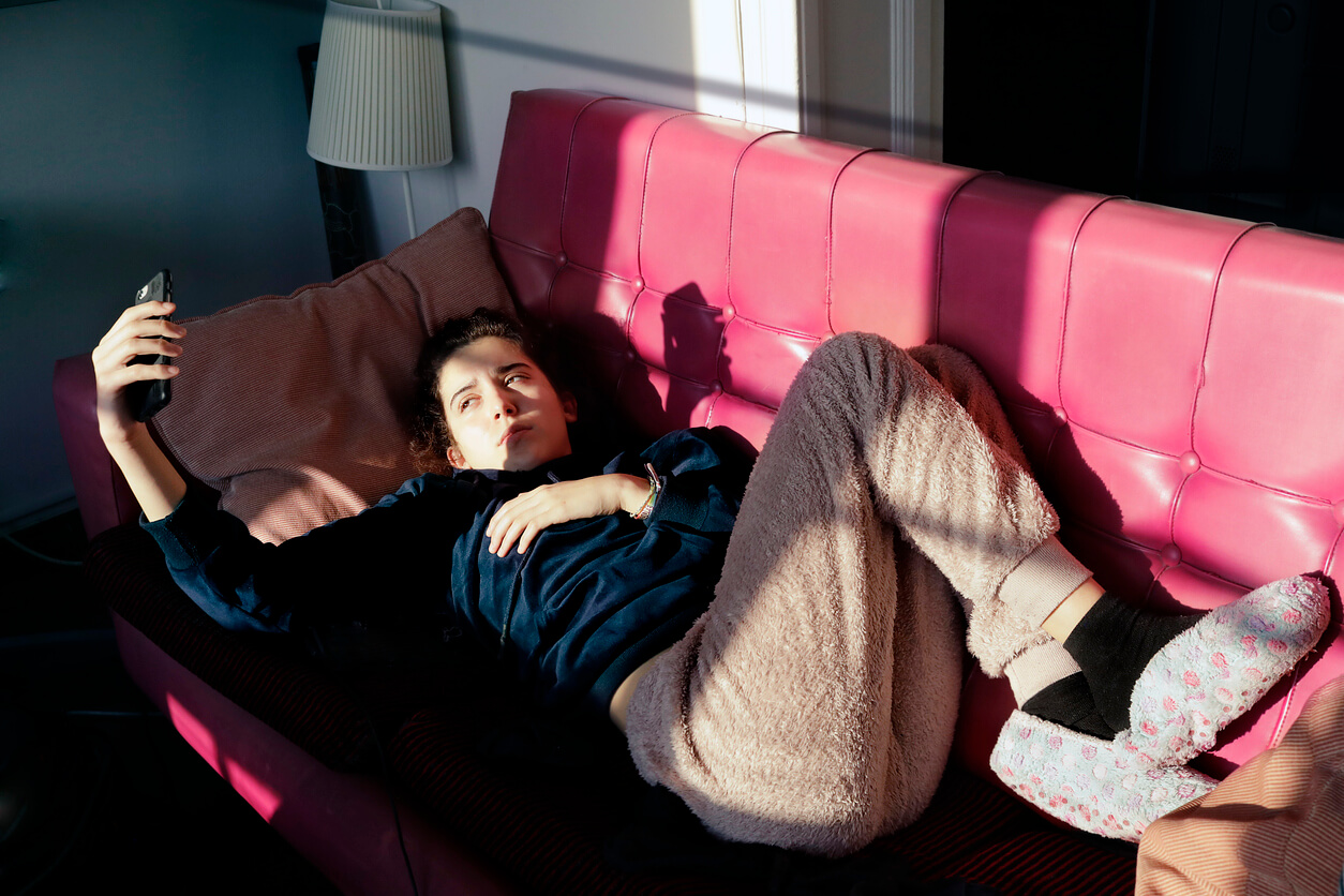 Une adolescente allongée sur un canapé avec un téléphone.