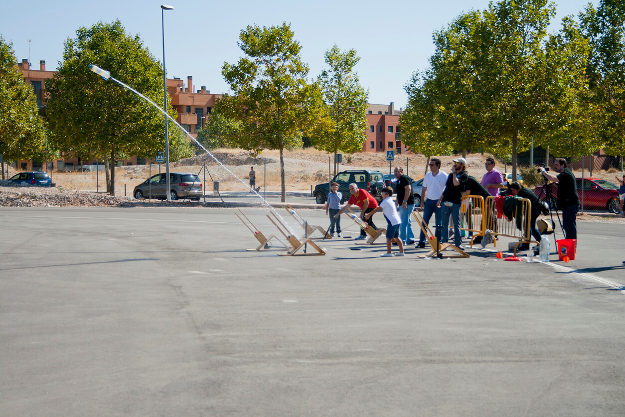Barn som sender raketter med vannflasker på en parkeringsplass.