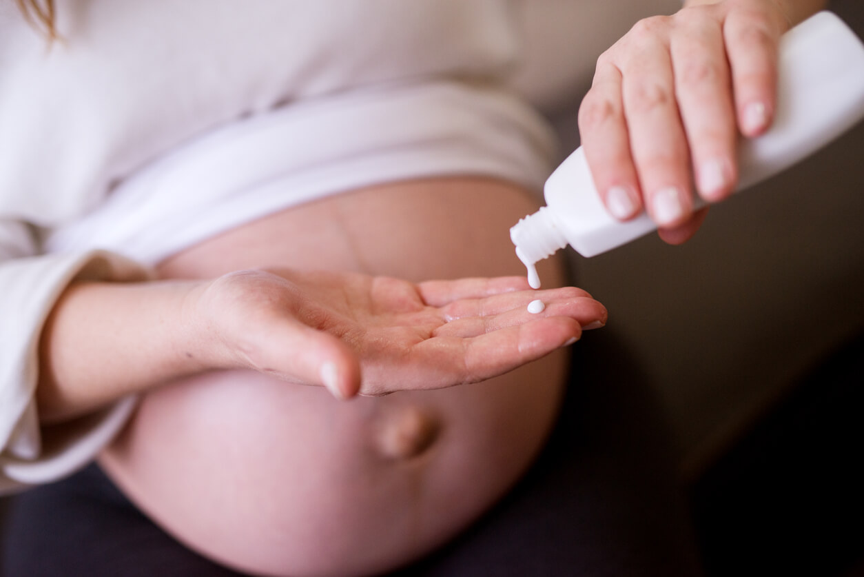 A pregnant woman pouring lotion onto her hand.