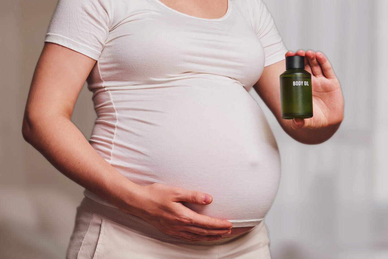 A pregnant woman holding a bottle of body oil.