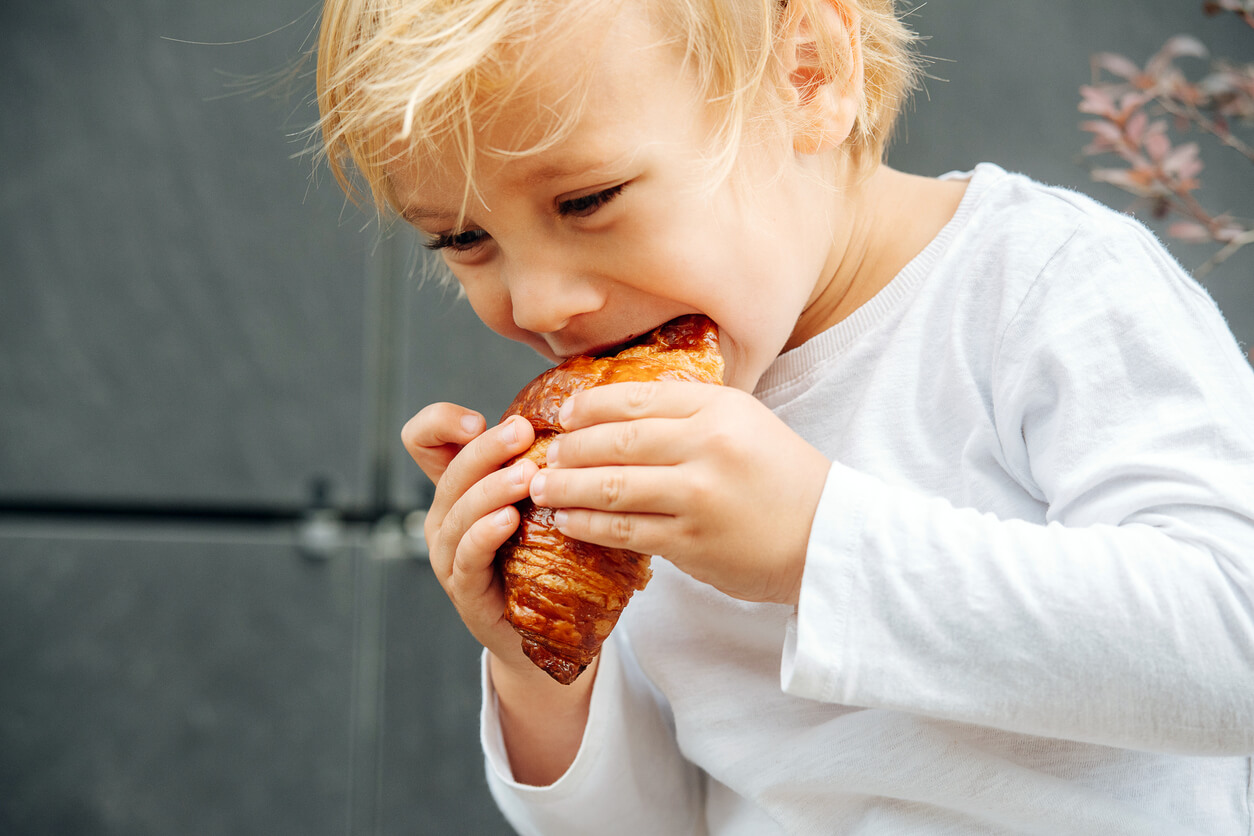 A toddler biting into a sweet croissant.