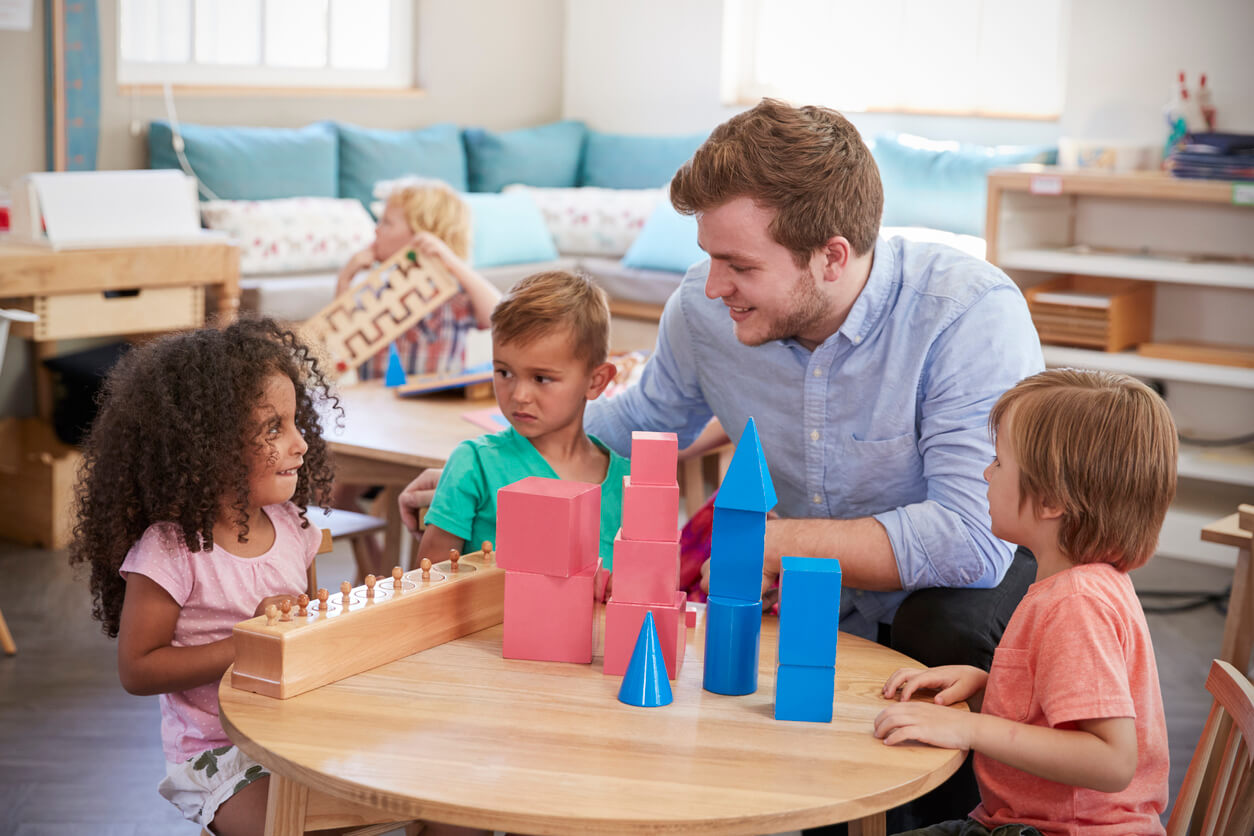 A teachers sitting at a small table with preschoolers playing with Montessori toys.