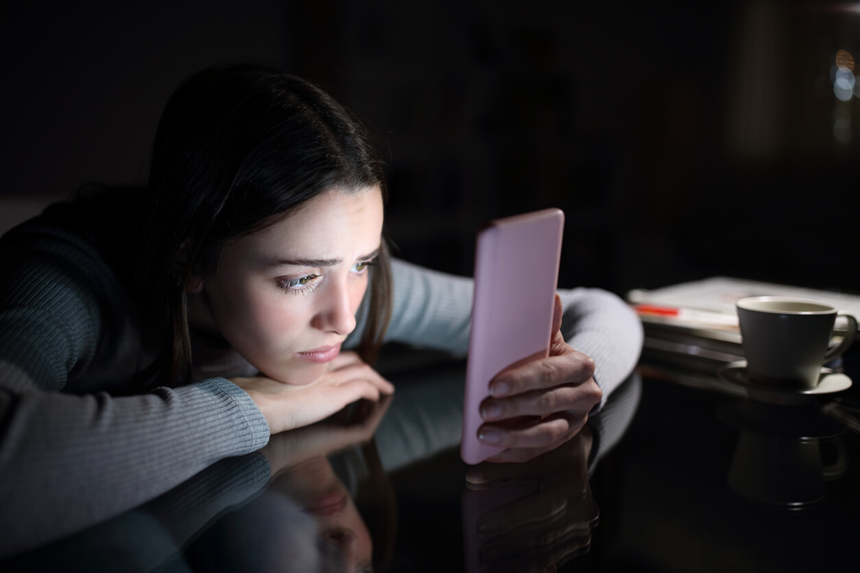 A teenage girl looking using her cell phone in the dark and looking overwhelmed.