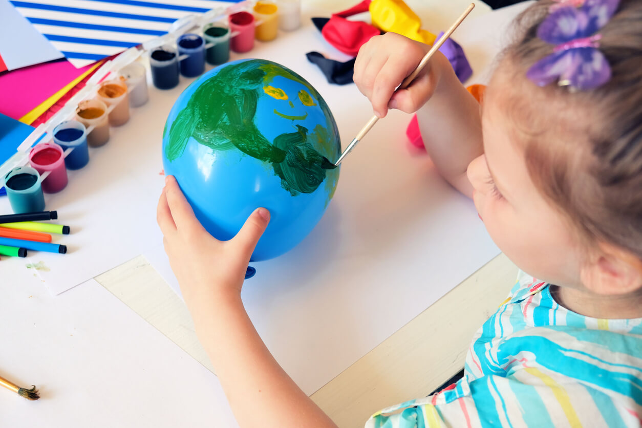 A little girl making a globe with a balloon and paint.