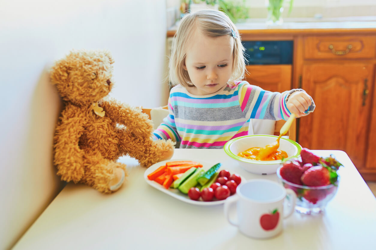 Ett litet barn sitter vid ett bord med färgglada frukter och grönsaker.