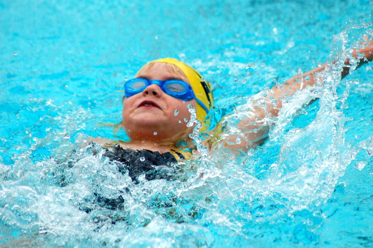 A young girl doing the backstroke in a pool.